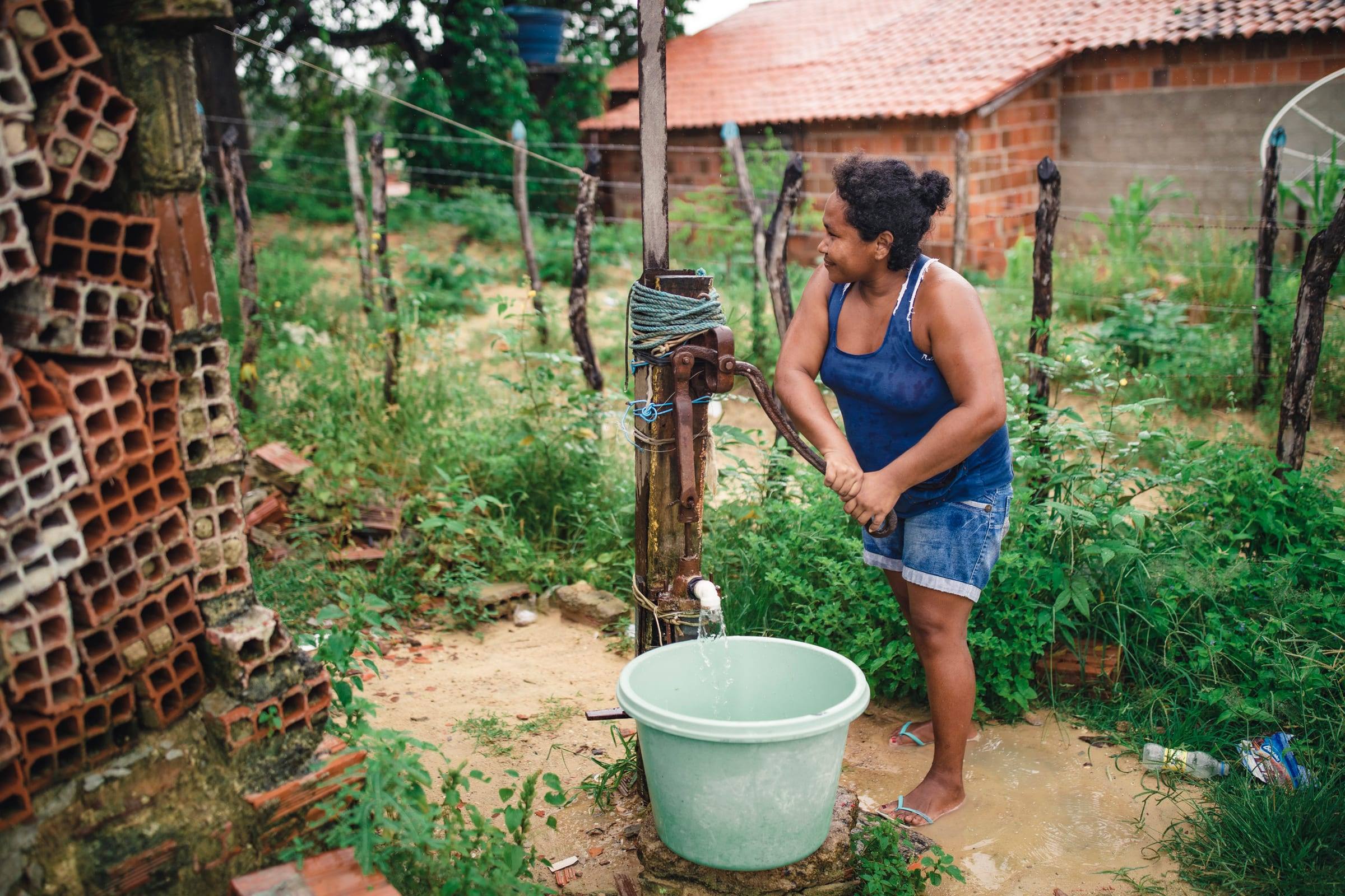 A woman pumps clean water into a bucket beside her home